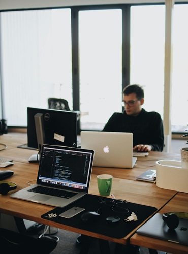 A web developer working on code in a modern office setting with multiple devices.